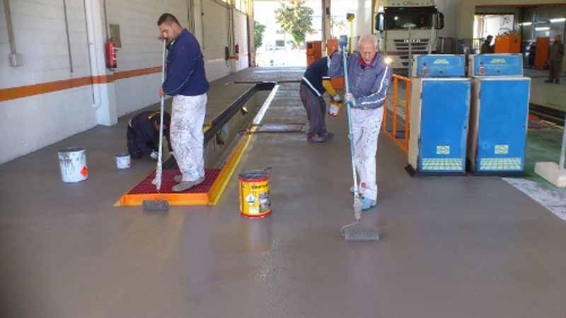 Dos hombres están pintando el suelo de un garaje.