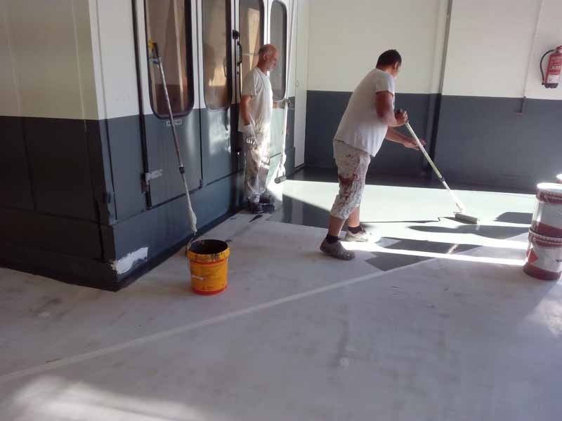 Dos hombres están pintando el suelo de un edificio.