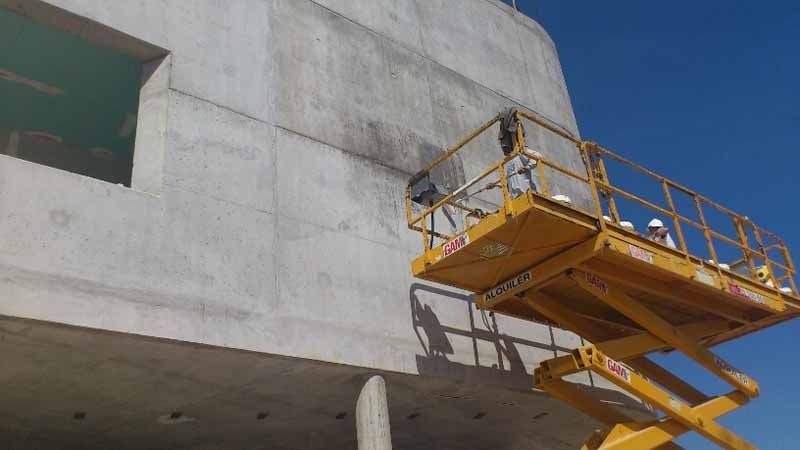 Un hombre está parado en un elevador de tijera frente a un edificio.