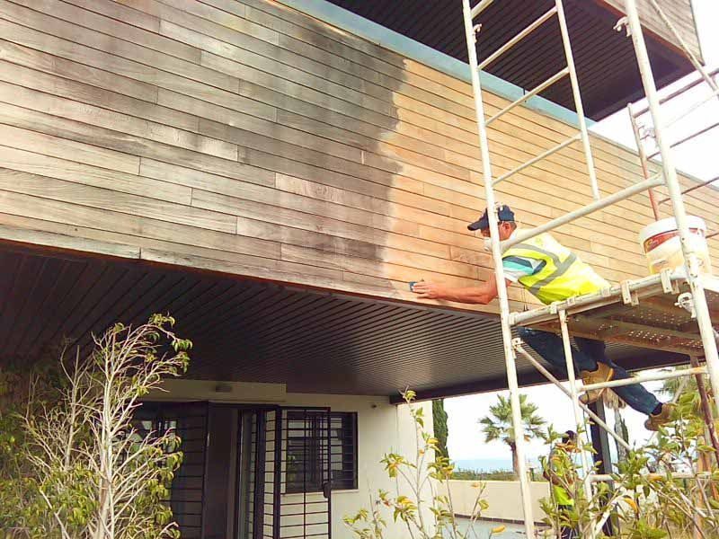 Un hombre está pintando el costado de un edificio sobre un andamio.