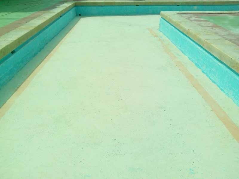 Una piscina con suelo de hormigón blanco y agua azul.