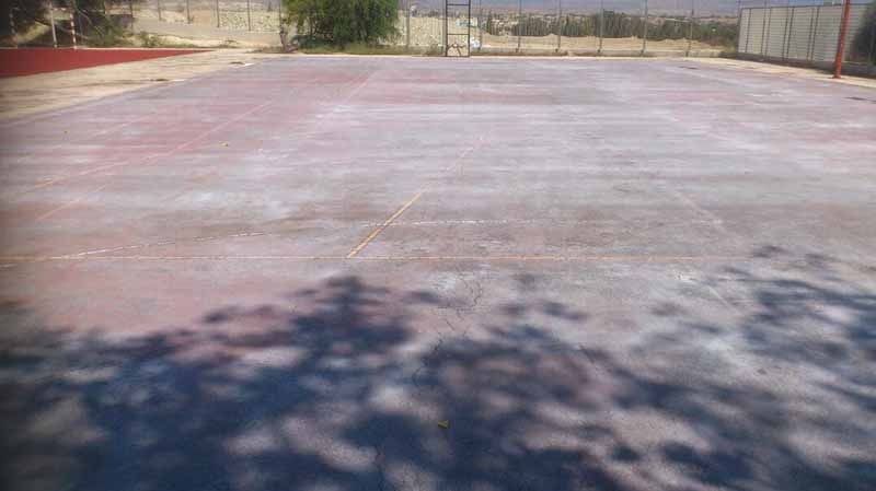 Una cancha de baloncesto con la sombra de un árbol en el suelo.