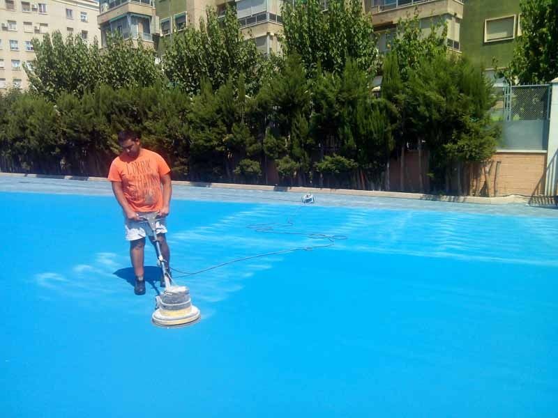Un hombre está limpiando una cancha de baloncesto azul con una máquina.