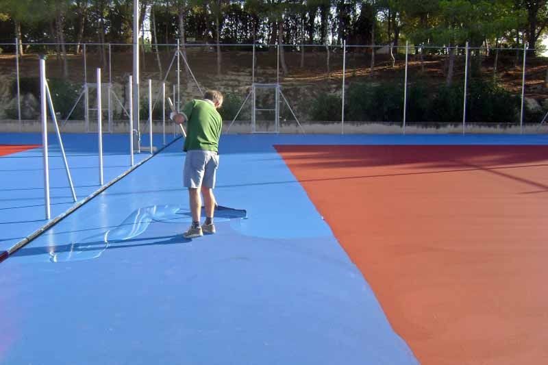 Un hombre está pintando una cancha de tenis con una escoba.