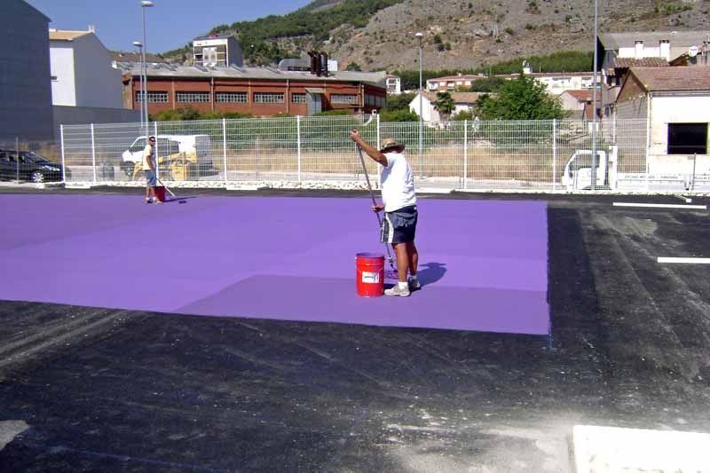 Un hombre está pintando una superficie morada con un barril rojo.