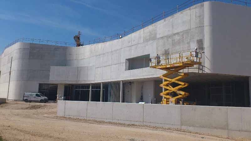 Un gran edificio en construcción con un elevador de tijera amarillo delante.