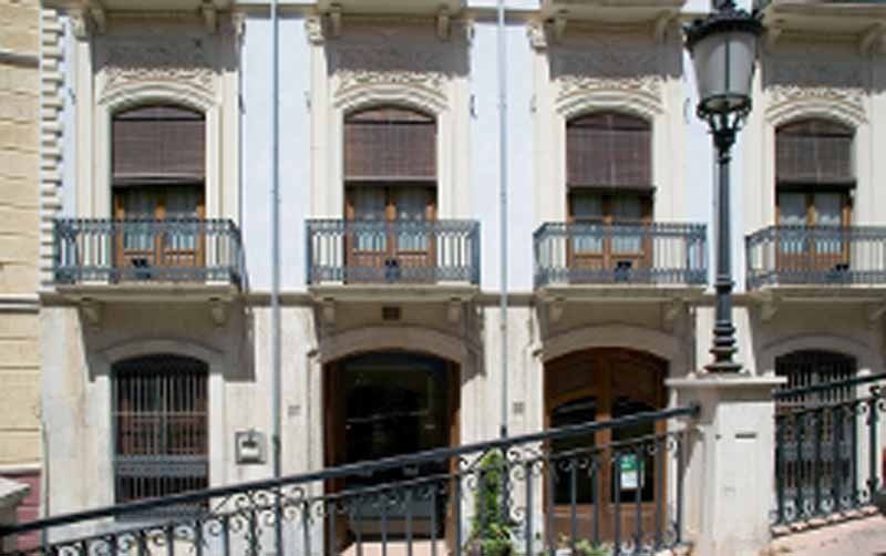 Un gran edificio blanco con balcones y una farola delante.