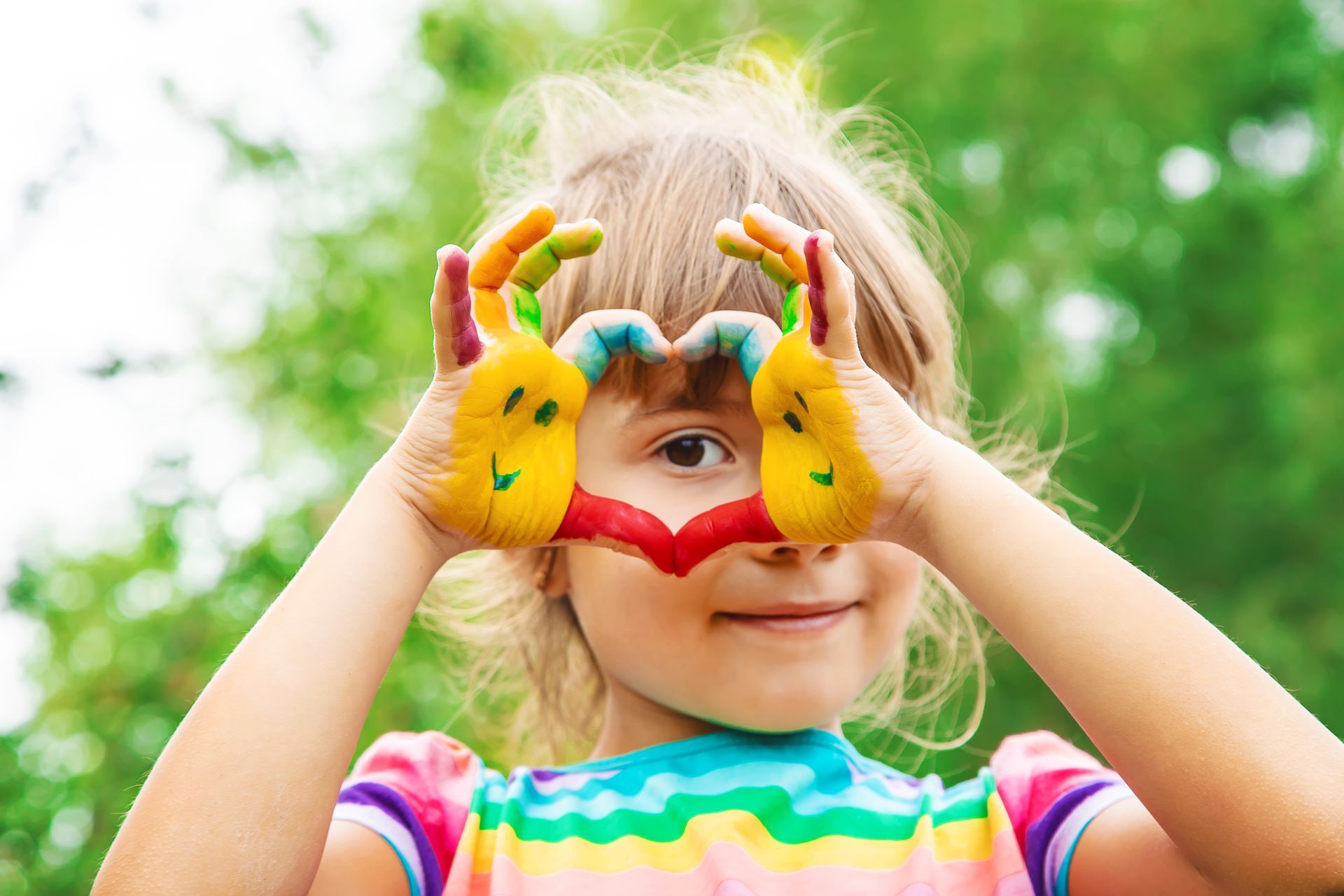 Enfant aux mains peintes formant un cœur, regardant à travers le centre.
