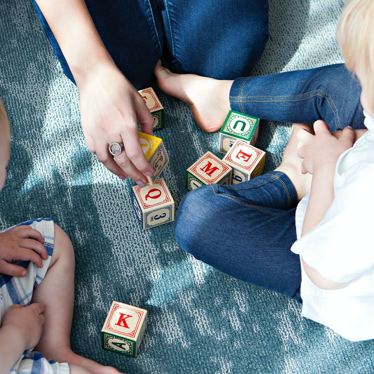 Personne et enfant jouant avec des blocs de l'alphabet sur un tapis bleu.