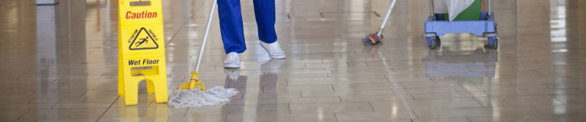 Une personne nettoie un sol brillant avec une serpillière ; un panneau  sol mouillé.
