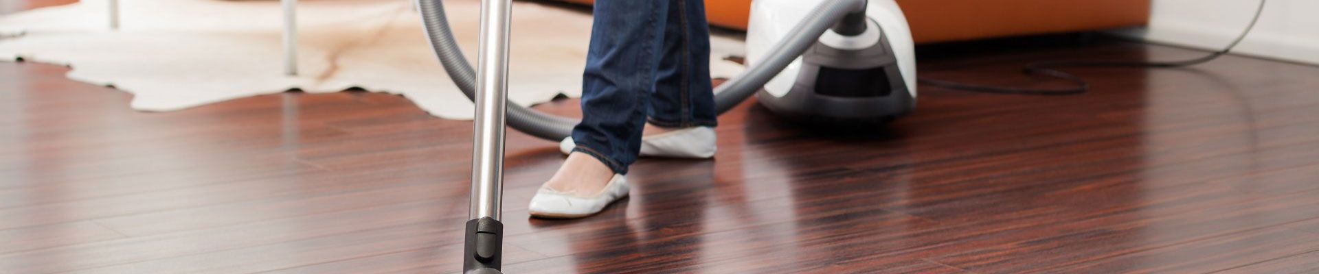 Une personne passe l'aspirateur sur un parquet foncé.