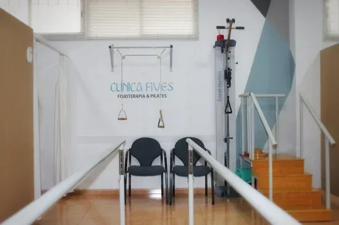 Interior de clínica de fisioterapia con equipos, sillas y escaleras; cartel