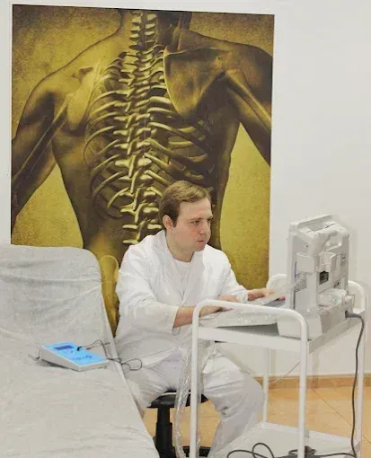 Hombre con bata blanca usando equipo médico, sentado en una clínica.