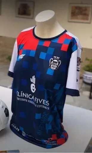 Camiseta de fútbol sobre maniquí; diseño azul marino, rojo y blanco; logotipo del patrocinador; emblema del equipo.