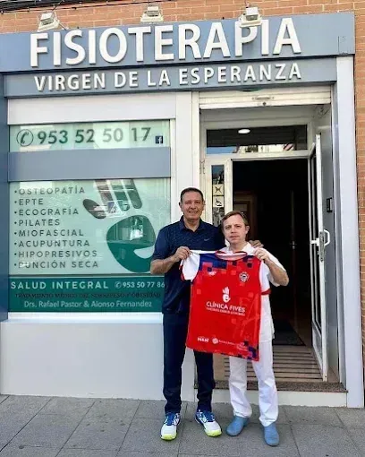 Dos hombres posan frente a una clínica de fisioterapia; uno de ellos sostiene una camiseta deportiva.