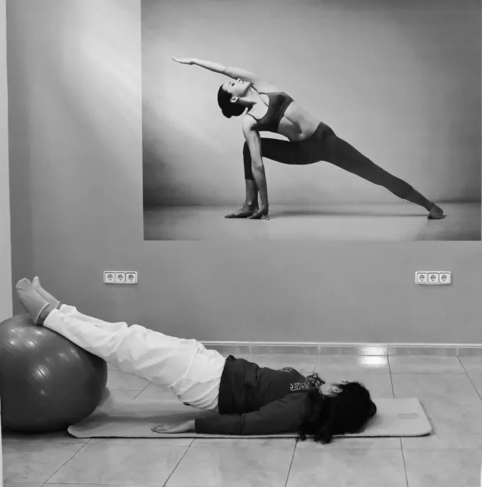 Instructor ayuda a una persona en una colchoneta durante una clase de ejercicios, con una imagen de una pose de yoga.