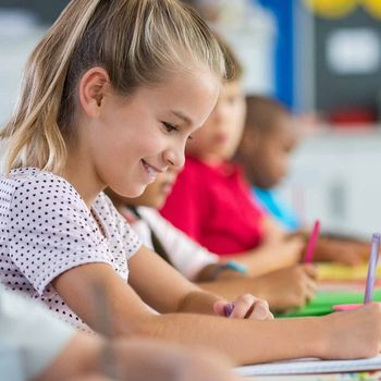 Eine Gruppe von Kindern sitzt an Schreibtischen in einem Klassenzimmer und schreibt in Hefte.