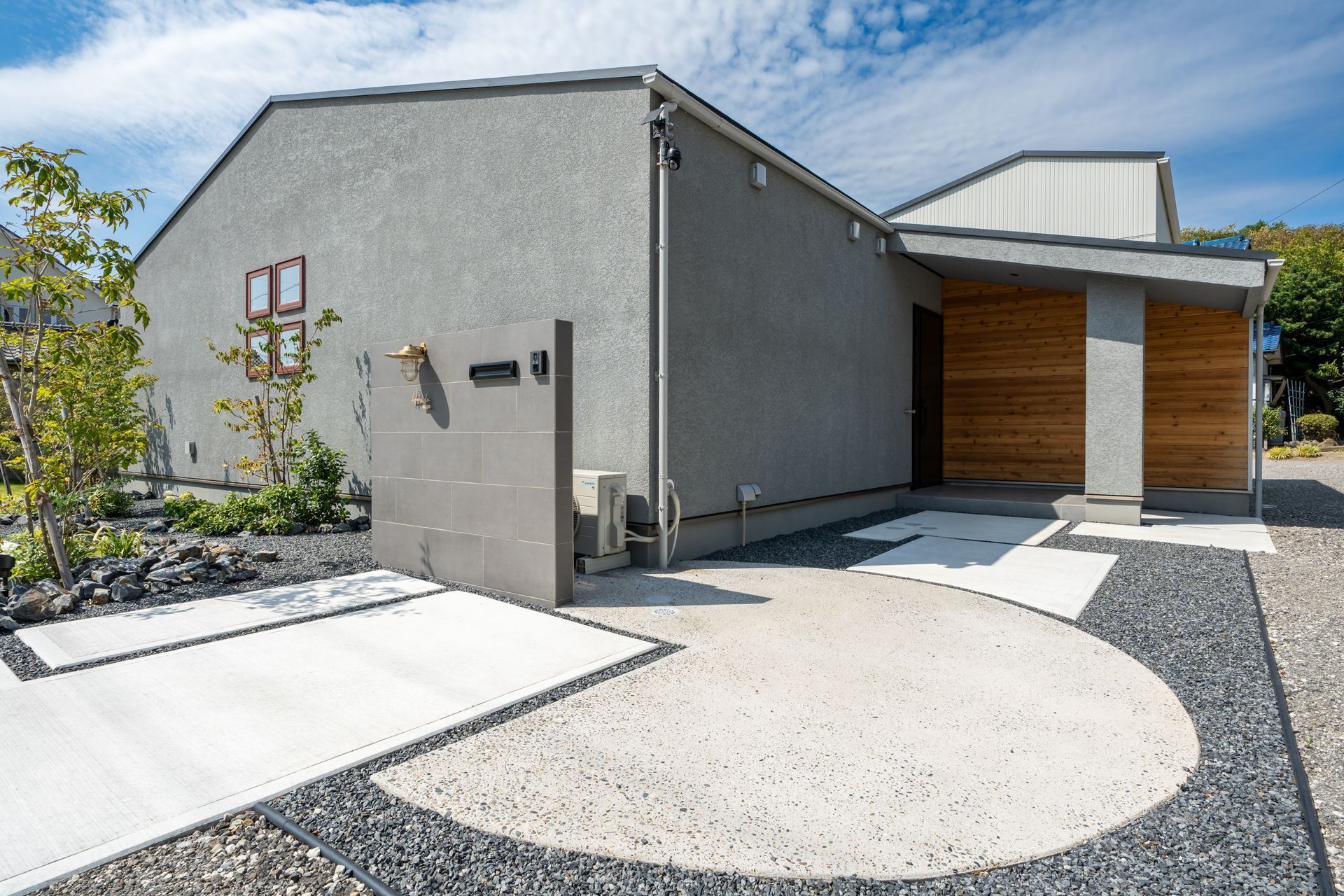 Maison moderne à l'extérieur gris, avec une allée de gravier incurvée et un porche en bois.