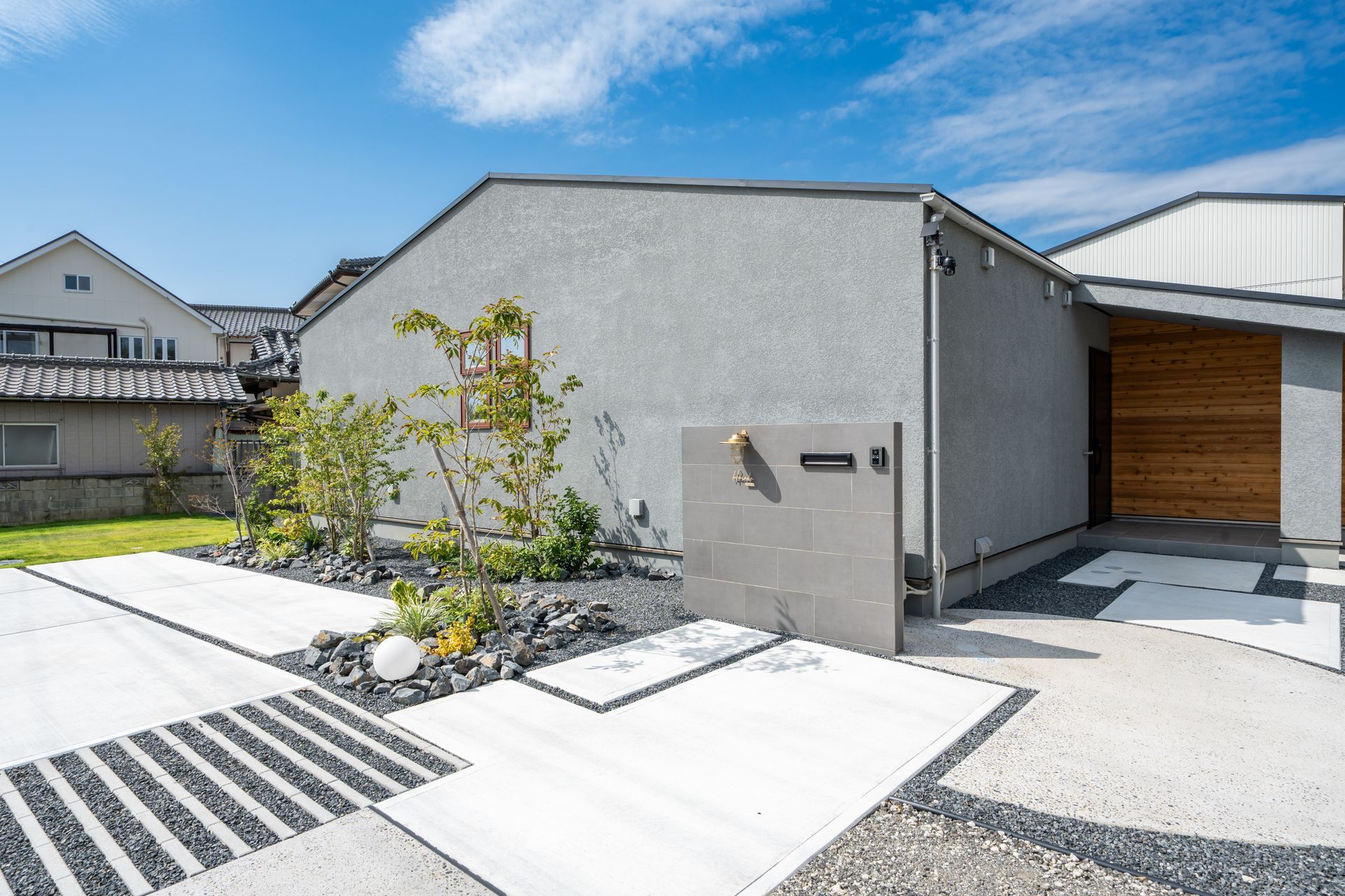 Maison moderne blanche avec allée en gravier, petit jardin et entrée en bois.