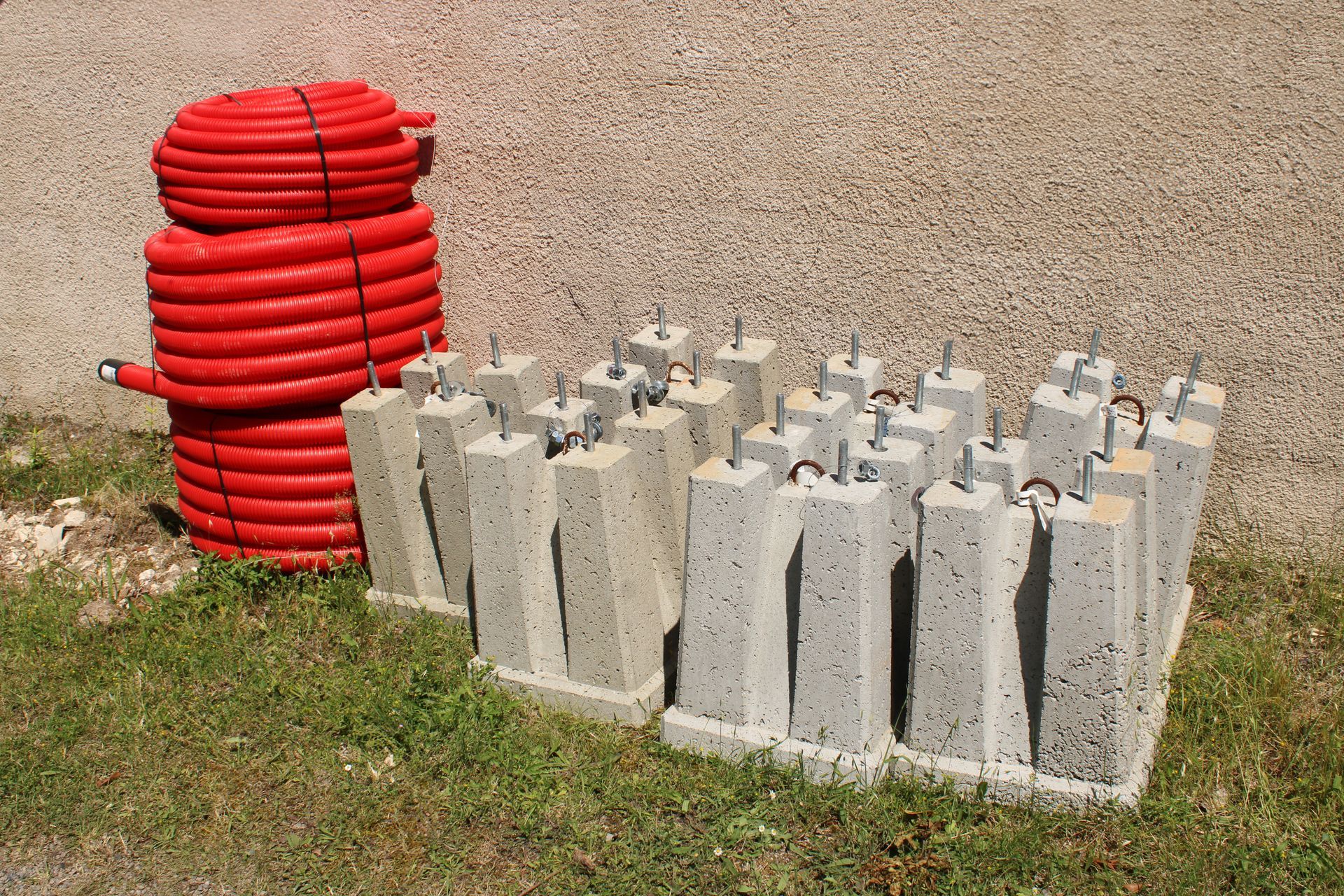 Des tubes rouges enroulés en spirale sont empilés à côté de rangées de blocs de béton gris, sur de l'herbe et du gravier.