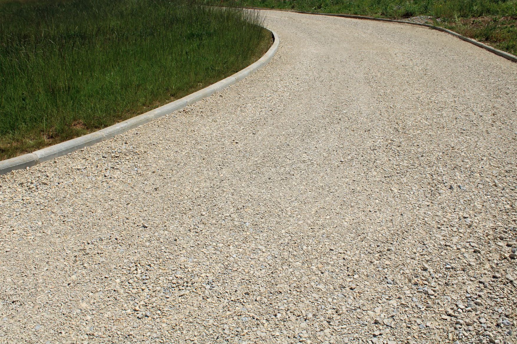 Chemin de gravier incurvé bordé de gazon et d'un rebord en béton