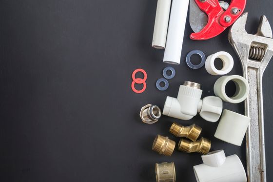 Divers petits accessoires et outils de plomberie éparpillés sur une surface sombre, avec des pièces rouges et argentées visibles.