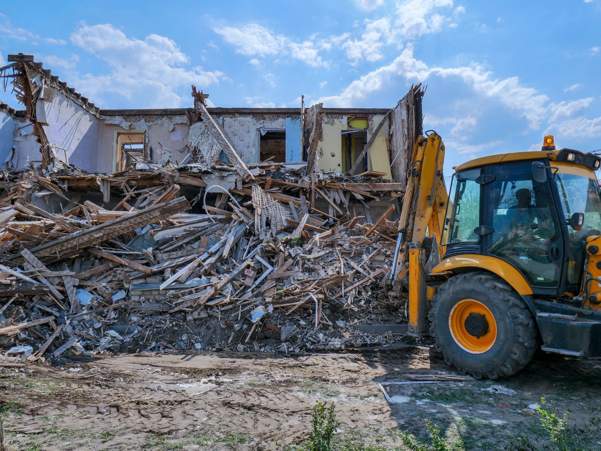 Une pelleteuse jaune à côté d'un bâtiment démoli, avec des décombres amoncelés sous un ciel nuageux.