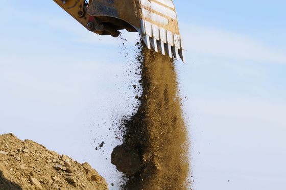 Godet d'excavatrice déversant de la terre sur un tas de terre, sur fond de ciel bleu.