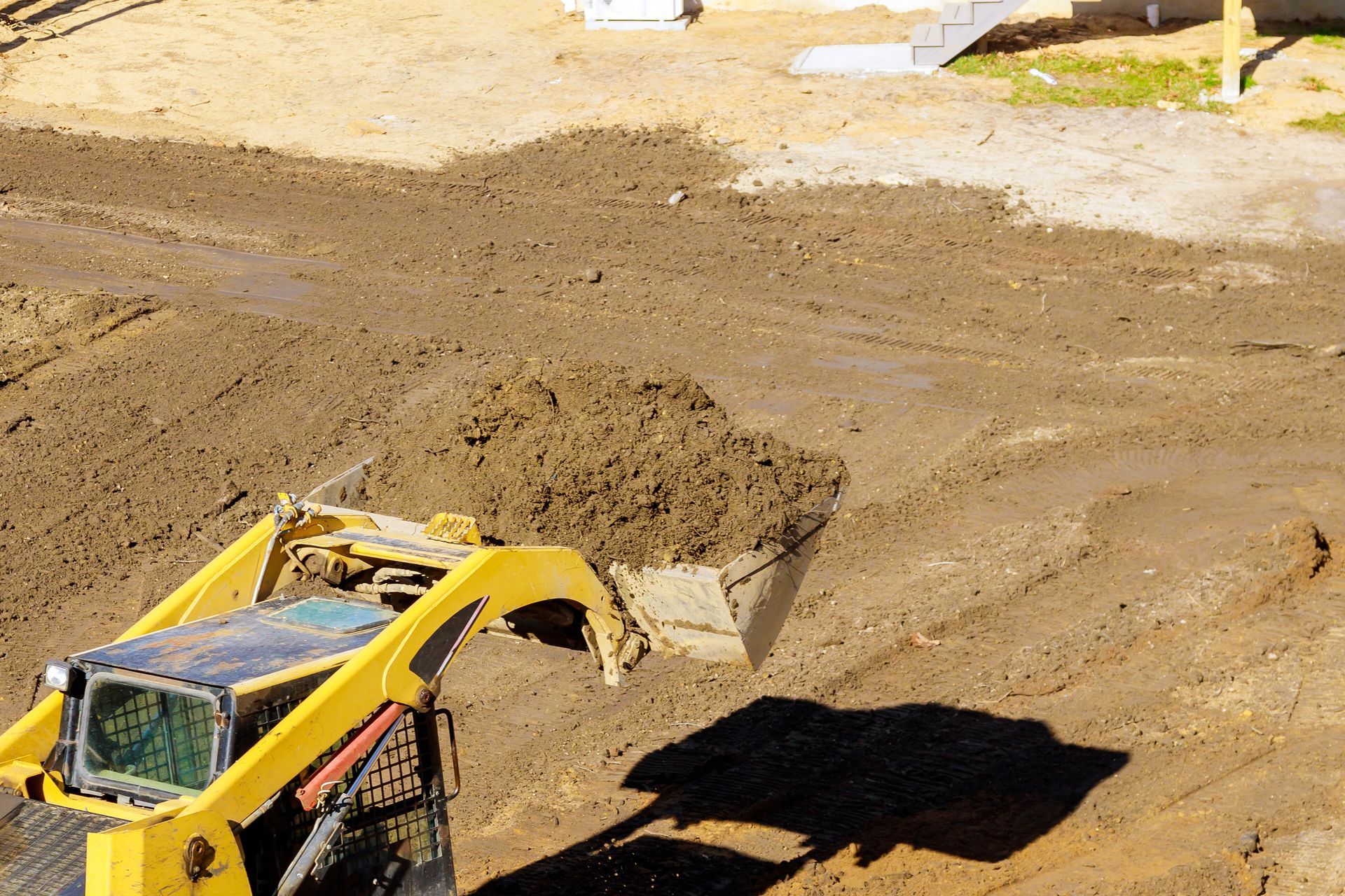 Un engin de chantier jaune déverse de la terre sur un chantier boueux.