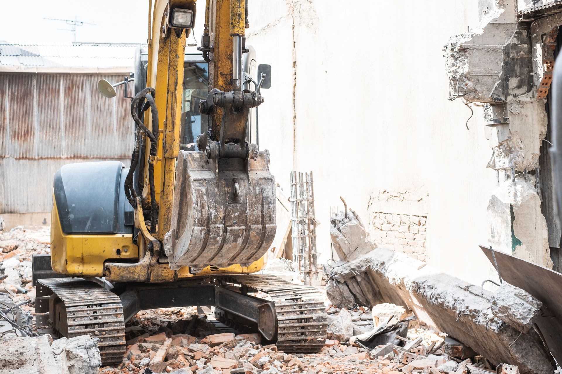 Une pelleteuse jaune démolit un mur en béton au milieu des décombres sur un chantier de construction
