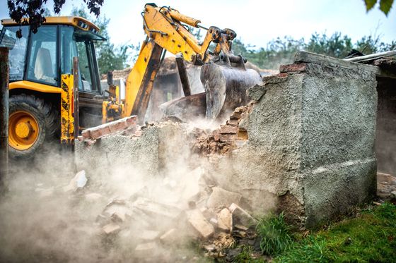 Une pelleteuse démolit un mur en béton dans un nuage de poussière sur un chantier de construction