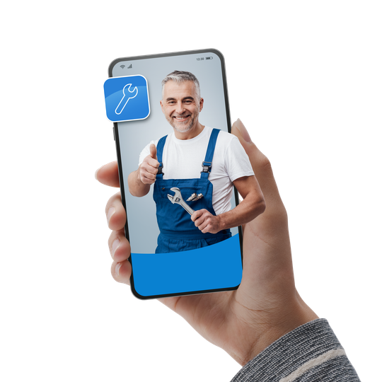 Une main tenant un smartphone montre un plombier souriant en salopette bleue faisant un signe de pouce levé.