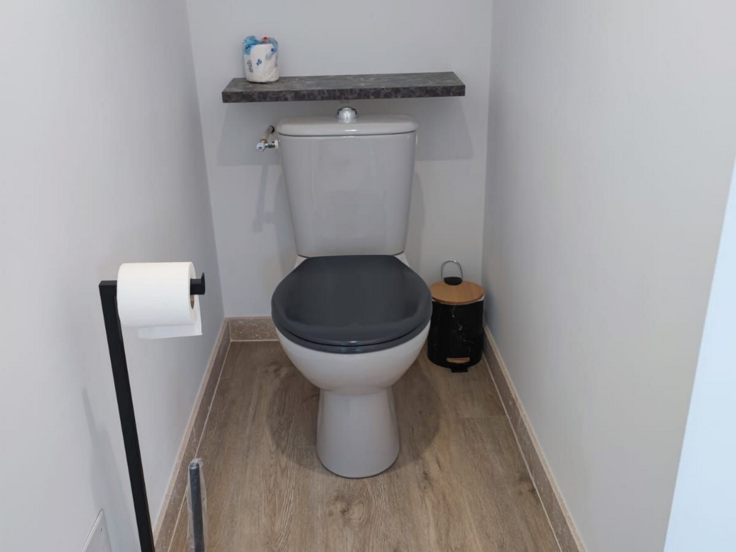 Toilette avec porte-papier toilette et étagère au-dessus du réservoir.