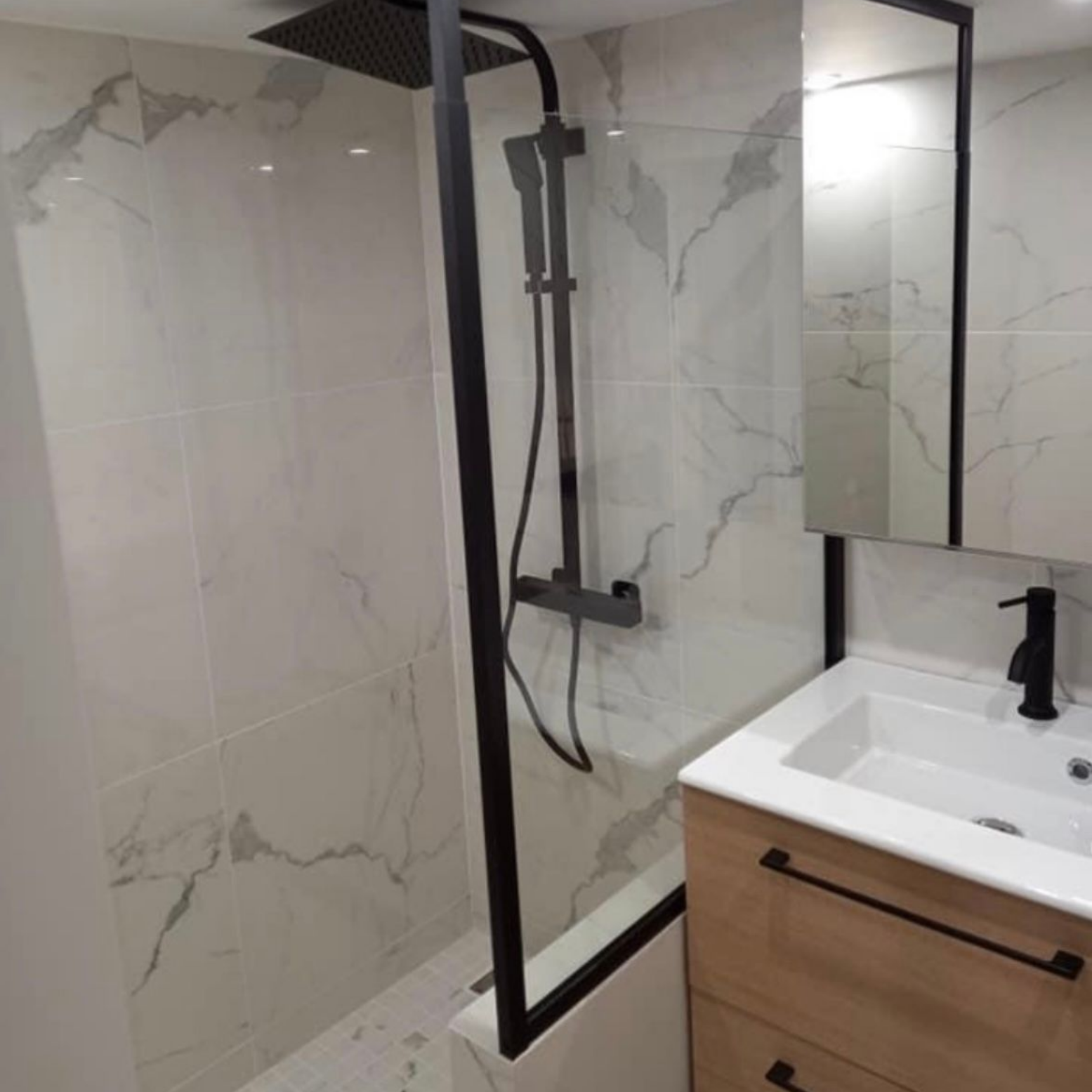 Salle de bains moderne avec paroi de douche en verre, carrelage imitation marbre et meuble-lavabo avec miroir.