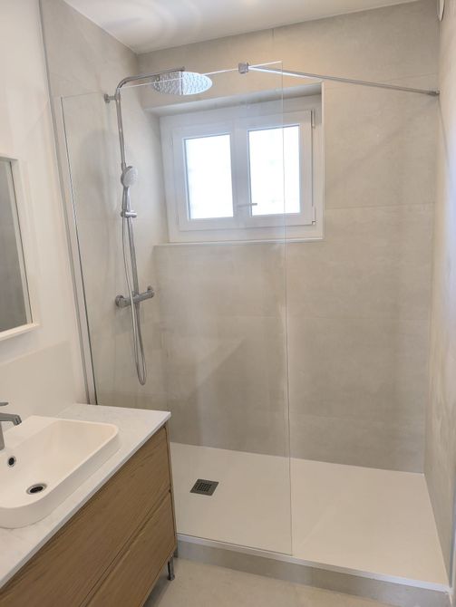 Salle de bains moderne avec douche à paroi de verre, murs carrelés blancs et petite fenêtre.