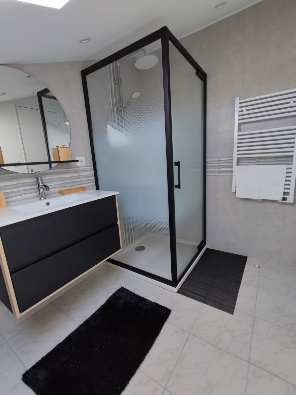 Salle de bains moderne avec cabine de douche en verre, meuble-lavabo, miroir mural et sol carrelé.