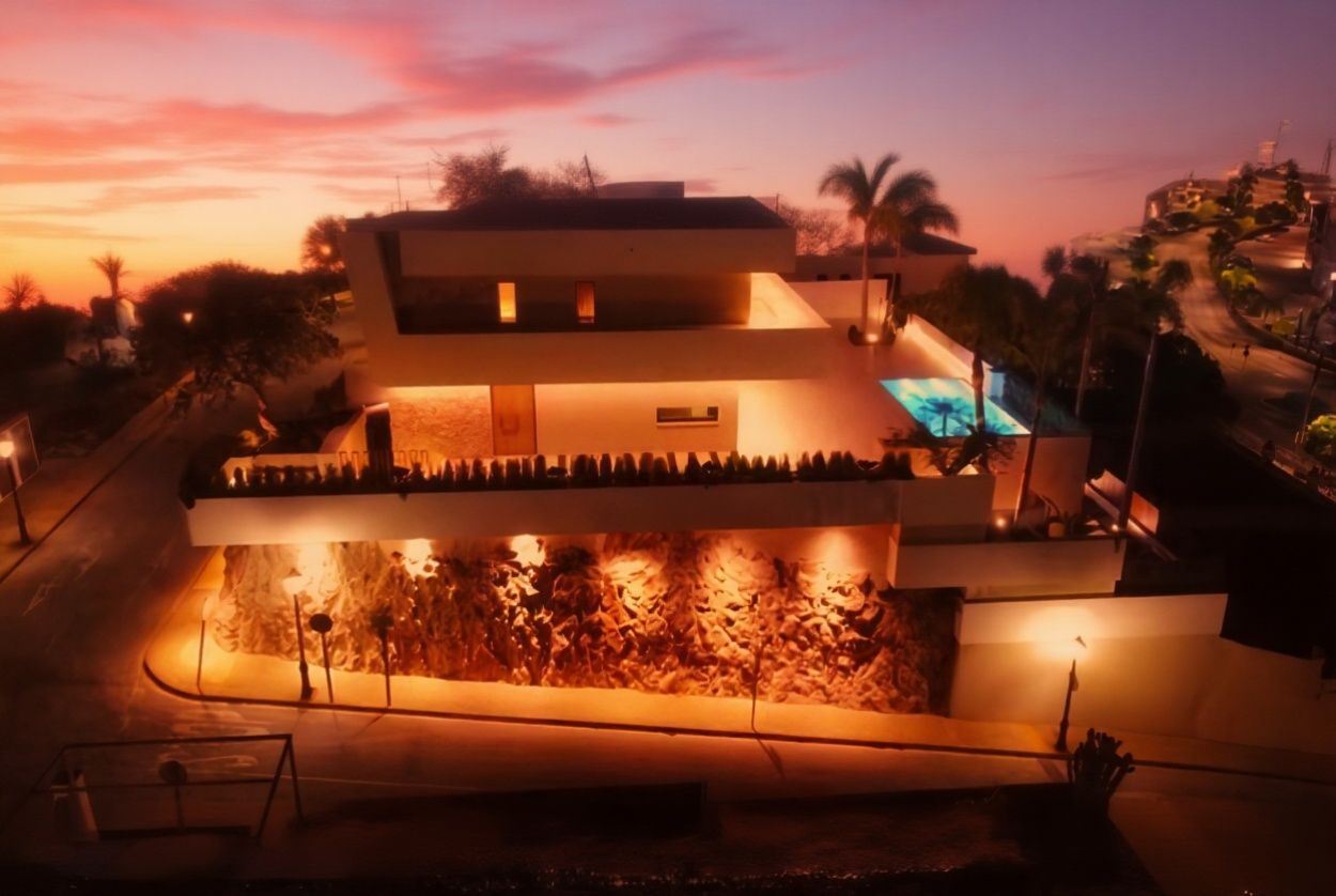 Casa moderna con luces exteriores iluminadas al atardecer, con piscina, palmeras y calle.