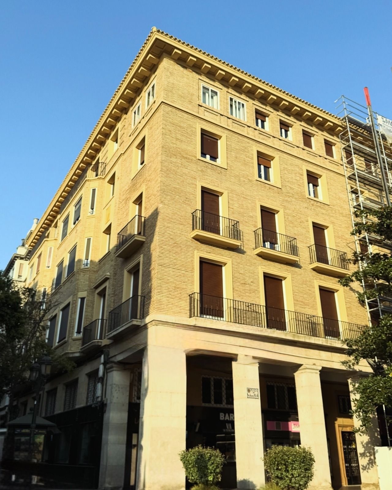 Edificio amarillo en esquina, bañado por el sol, con balcones contra un cielo azul despejado.