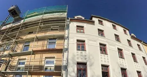 Andamios en un edificio de apartamentos color crema junto a una fachada blanca bajo un cielo azul claro.