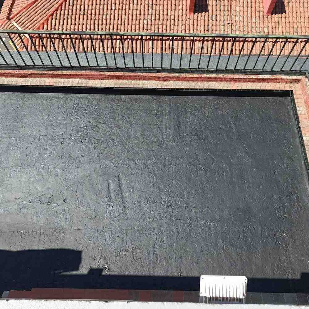 Un trabajador aplica con brocha una capa impermeabilizante negra a una azotea plana.