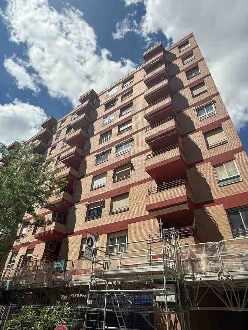 Un trabajador con chaleco naranja pinta el exterior de un edificio desde un andamio.