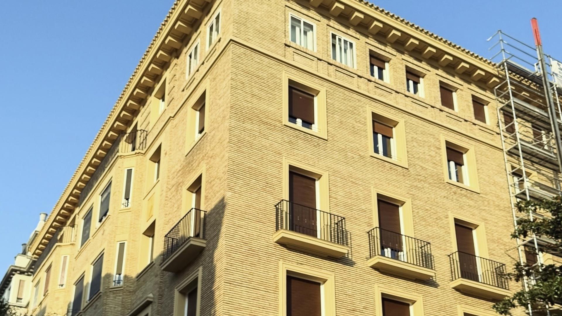 Andamios en un edificio de apartamentos color crema junto a una fachada blanca bajo un cielo azul claro.