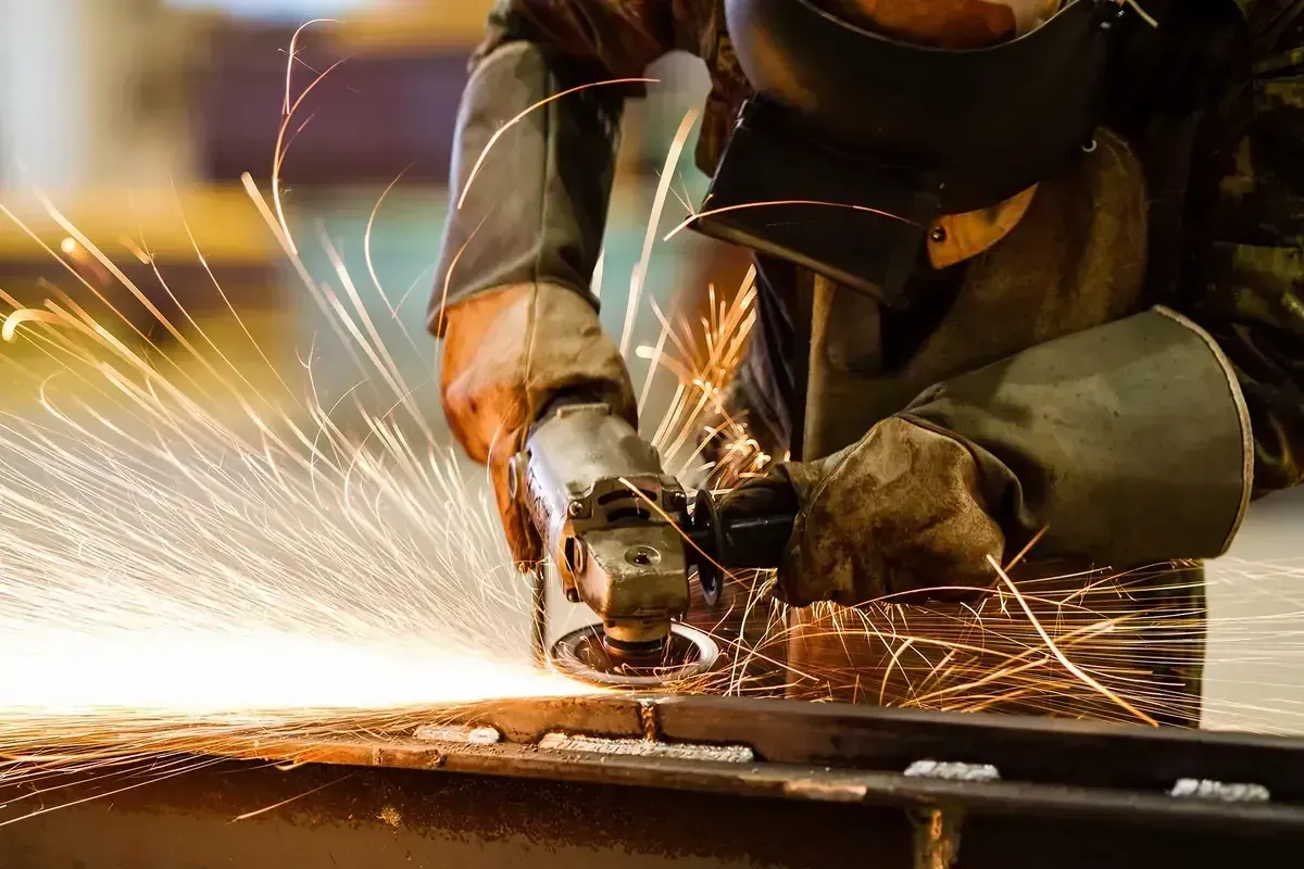 Un trabajador utiliza una amoladora angular sobre metal, generando chispas brillantes en la superficie del taller.