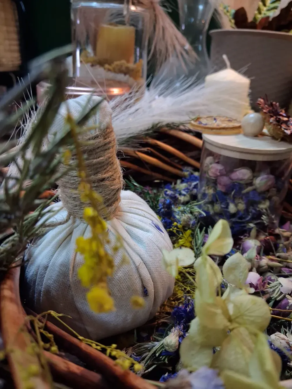 Productos de spa a base de hierbas, que incluyen compresas, velas, flores secas y especias, en un entorno natural.