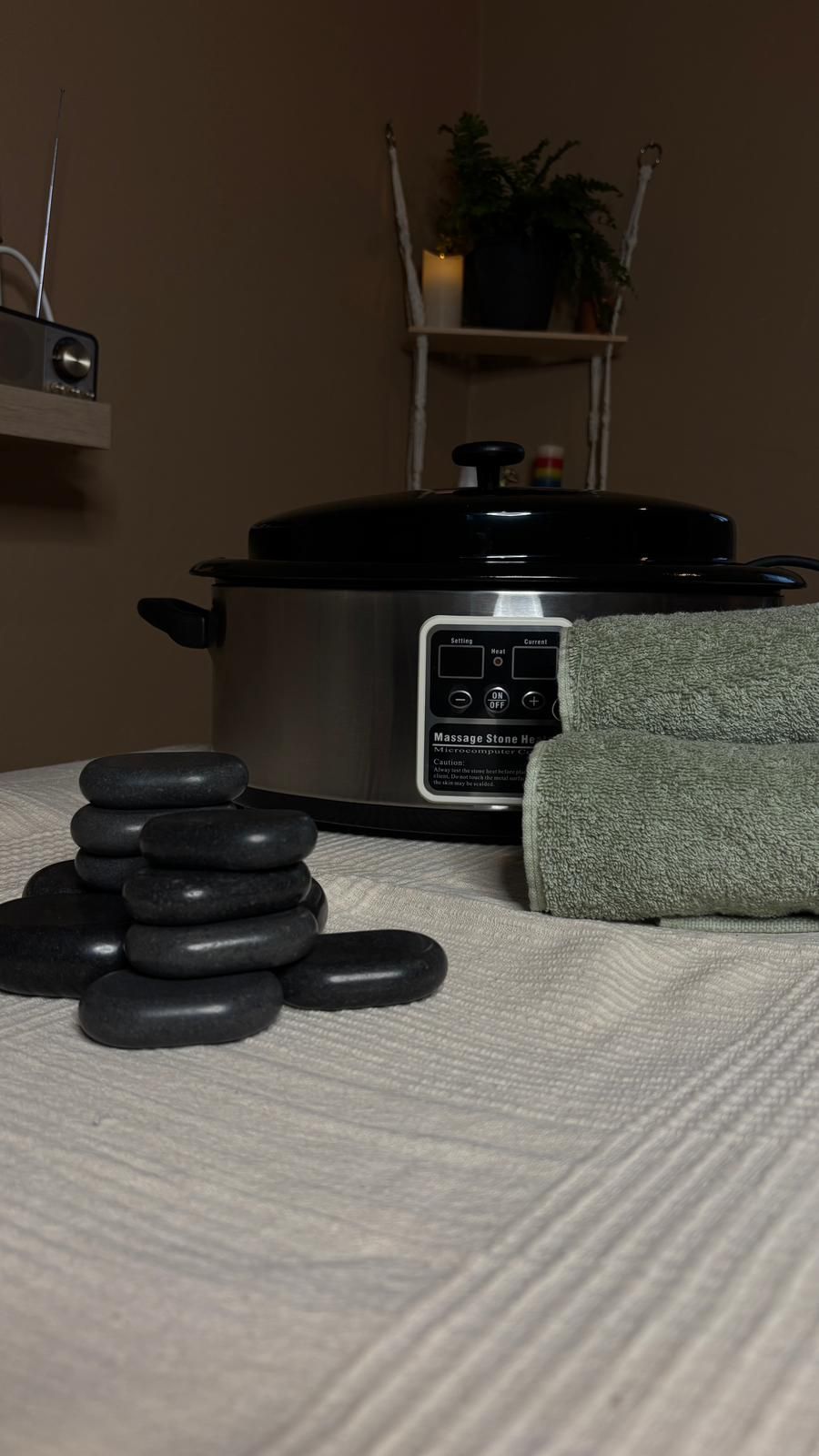 Configuración de masaje con piedras calientes: piedras apiladas cerca de una olla de calentamiento con una toalla.