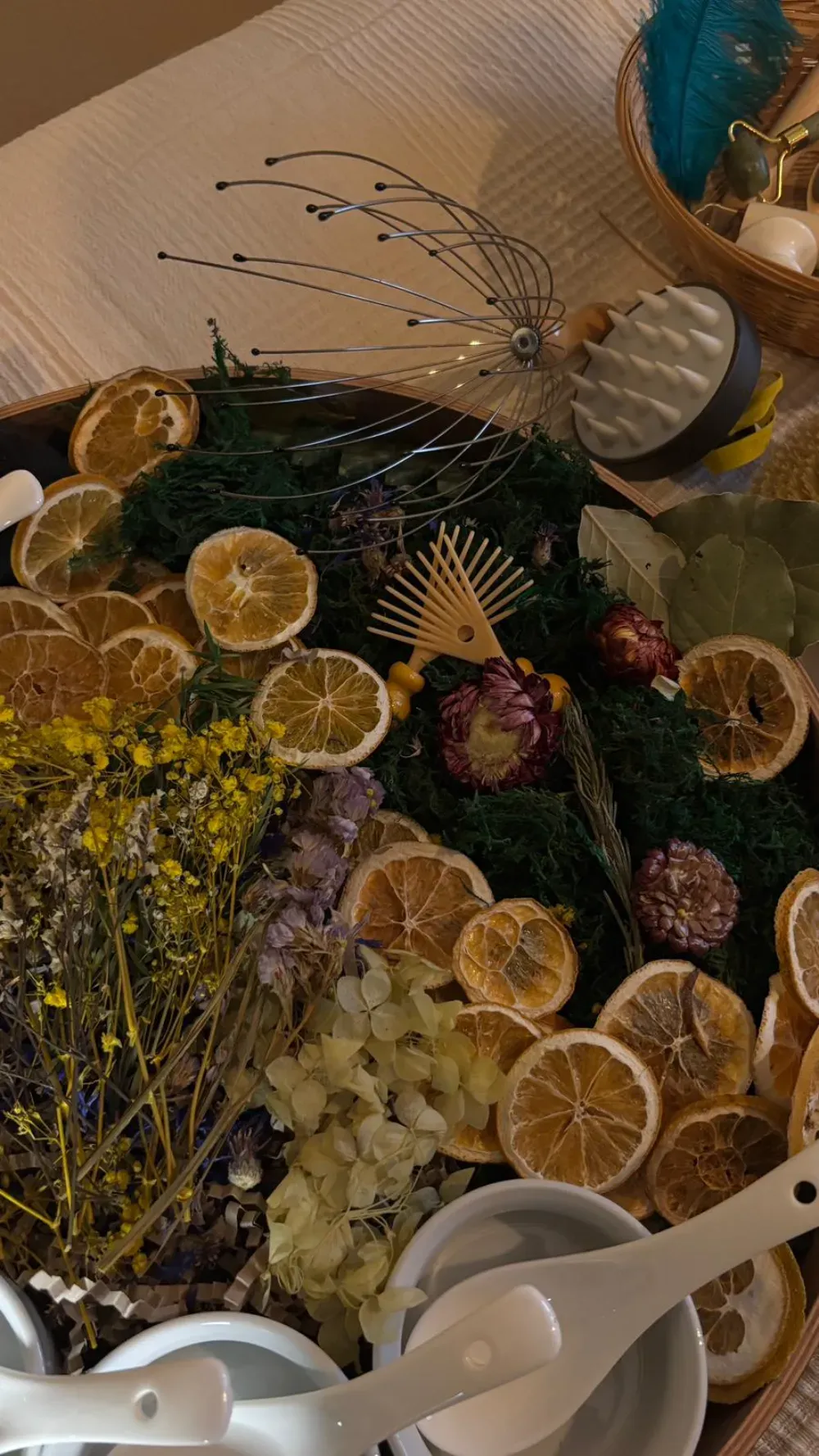 Fotografía cenital de una bandeja con naranjas secas, flores, hierbas y elementos decorativos. Cuencos blancos con cucharas.