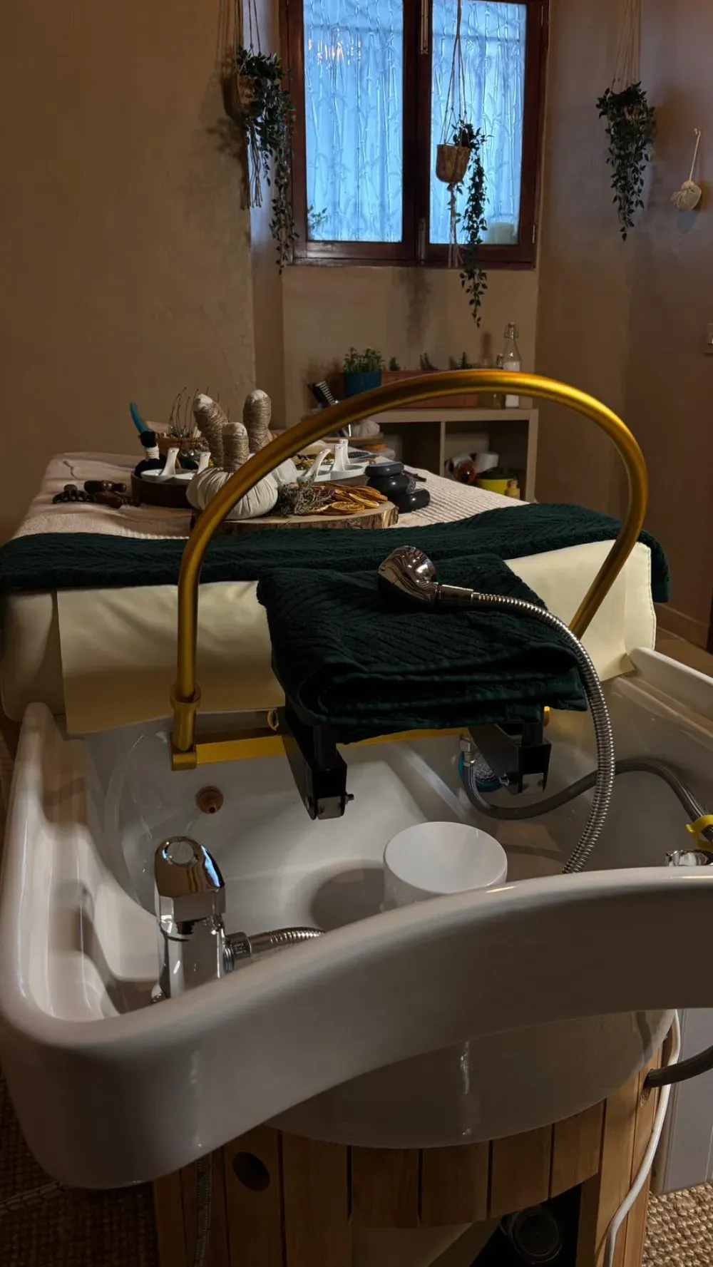 Interior del salón: Spa para pies con marco dorado, mesa de tratamiento y plantas junto a una ventana.