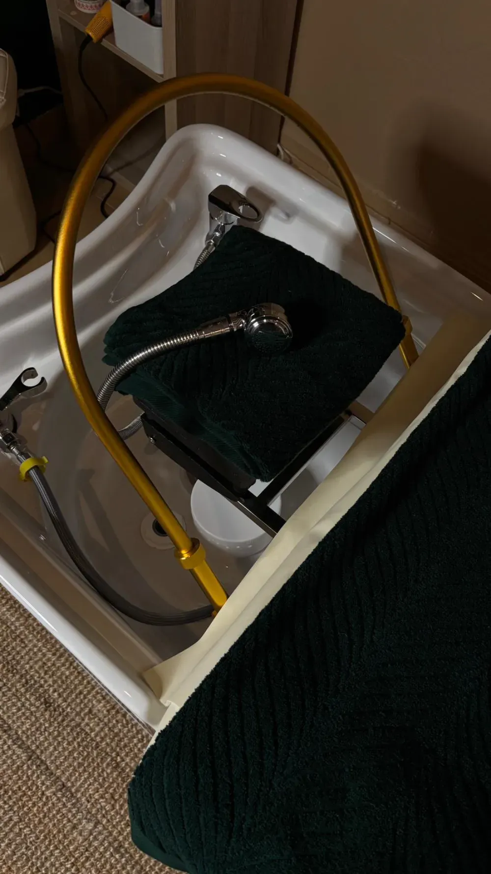 Un spa para pies blanco con soporte dorado, toalla verde oscuro y cabezal de ducha.