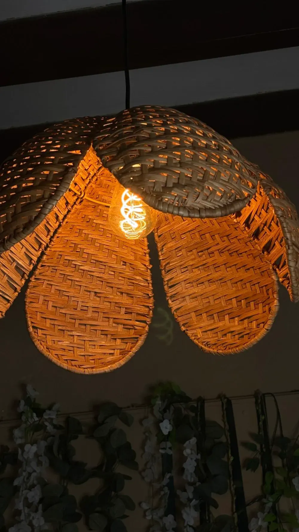 Lámpara colgante tejida en forma de flor con bombilla de filamento expuesto que emite una cálida luz.