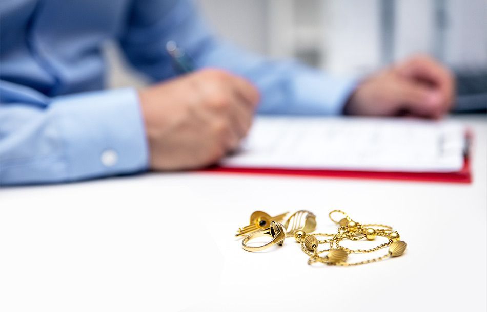 Professionnel signant un document sur un bureau sur lequel repose des bijoux en or
